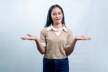 İki eli yanda duran neşeli Endonezyalı kadın seçenekler sunuyor ya da beyaz bir arka planda gülümseyerek şüphe gösteriyor..