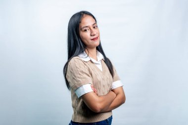 Kendine güvenen, sıradan giyinmiş, kollarını çapraz açı yaparak kurnazca gülümseyen genç bir Asyalı kadın. Parlak beyaz bir arkaplanda izole edilmiş.