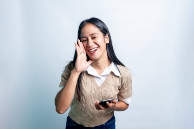 Neşeli, genç bir Asyalı kadın bir mesaj fısıldıyor ya da bağırıyor. Elinde akıllı bir telefon var. Beyaz arkaplanda izole.