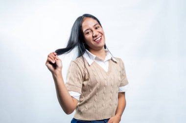 Saçlarıyla oynayan mutlu Endonezyalı genç kadın. Neşenin ve güzelliğin özgün ifadesi, temiz beyaz bir arkaplanda günlük şık kıyafetler giymek..