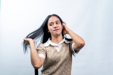 Endonezyalı güzel bir kadının portresi uzun ve sağlıklı saçlarına dokunuyor ve onları düzeltiyor. Beyaz arka planda saç bakımı, güzellik ve güven kavramı.