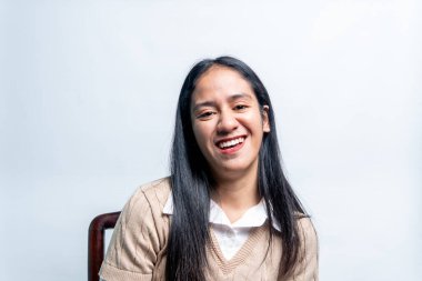 Mutlu Güneydoğu Asyalı kadın gülüyor, beyaz bir gömleğin üzerine bej bir kazak giyiyor. Temiz beyaz bir arkaplanda mutluluğun otantik ifadesi.