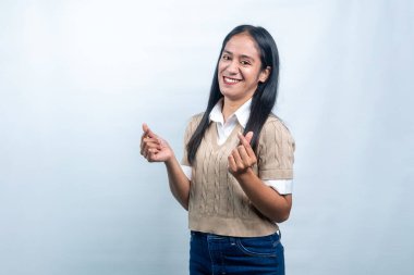 Endonezyalı neşeli genç bir kadın gülümseyerek parmaklarıyla küçük kalp işaretleri yapıyor. Aşkı, takdiri ve K-pop kültür eğilimlerini temsil ediyor..