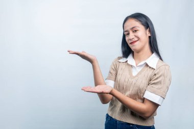 Endonezyalı mutlu genç bir kadın bir ürün ya da metin sunar gibi ellerini uzatıyor. Reklamlar, pazarlama ve web pankartları için ideal.