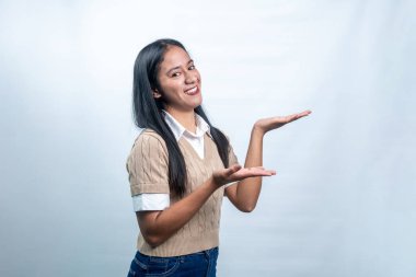 Endonezyalı mutlu genç bir kadın bir ürün ya da metin sunar gibi ellerini uzatıyor. Reklamlar, pazarlama ve web pankartları için ideal.