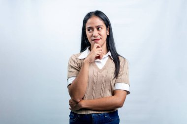 Düşünceli bir ifadeyle genç bir Endonezyalı kadın, çenesini tutuyor ve yana bakıyor, karar verme, planlama ya da merakı temsil ediyor..