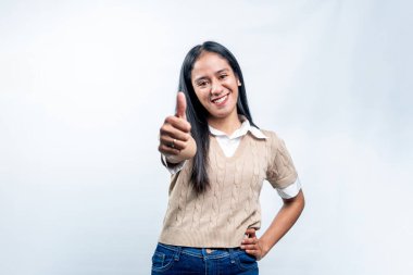 Gülümseyen genç Endonezyalı bir kadın kameraya doğru başparmak kaldırıyor. Anlaşmayı, tavsiyeyi, başarıyı ve olumlu geri bildirimi dile getiriyor..