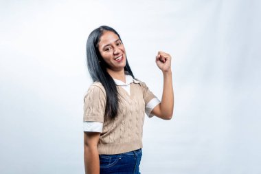 Neşeli genç Güneydoğu Asyalı kadın gülümseyip yumruğunu kaldırıyor. Başarılı bir jestle zaferi veya başarıyı beyaz bir arkaplanda kutluyor..