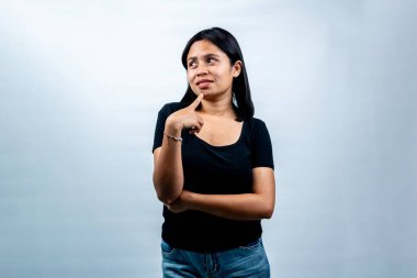 Düşünceli bir ifadeyle genç Endonezyalı bir kadının portresi, çenesine dokunuyor ve beyaz bir stüdyonun arka planına yan bakıyor..