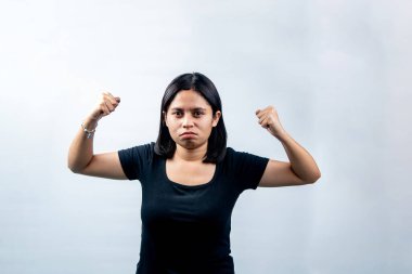 Kararlı genç bir Asyalı kadının portresi beyaz arka plana karşı ciddi ve güçlü bir ifadeyle kaslarını esnetiyor..