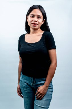 Dost canlısı ve doğal bir ifadeyle genç bir Asyalı kadın, beyaz bir stüdyo geçmişine karşı siyah gömlek ve kot pantolon giyiyor..