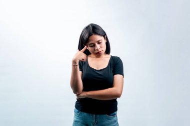 Siyah tişörtlü stresli Endonezyalı bir kadının portresi beyaz arka planda izole edilmiş, aşağıya bakıyor ve şakağına dokunuyor..