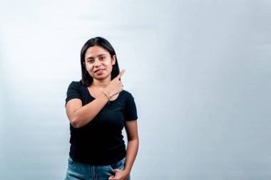 Siyah tişörtlü arkadaş canlısı Endonezyalı bir kadının portresi beyaz arka planda izole edilmiş, boş bir yeri işaret ediyor..