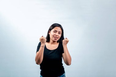 Siyah tişörtlü, mutlu bir Endonezyalı kadının portresi beyaz arka planda izole edilmiş yumruklarıyla kutlama ve tezahürat yapıyor..