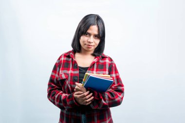 Kırmızı ekose gömlekli Endonezyalı dost canlısı bir kadın elinde defterler tutuyordu. Beyaz bir arkaplanda izole edilmiş yüksek kaliteli bir öğrenci portresi..