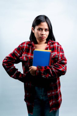 Kırmızı ekose gömlekli, kendine güvenen genç bir Güneydoğu Asyalı kadının portresi. Bir eli kalçasında ve düz bir arkaplanda defterleri tutuyor..