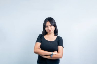 Siyah gömlekli, kolları çapraz genç bir Güneydoğu Asyalı kadının portresi. Açık gri arka planda izole edilmiş özgüvenli bir stüdyo çekimi..