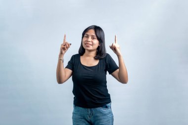 Siyah gömlekli genç Güneydoğu Asyalı kadın kameraya bakıyor ve yukarı bakıyor. Açık gri arkaplanda izole edilmiş bir stüdyo portresi.