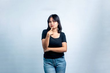 Siyah gömlekli genç bir Güneydoğu Asyalı kadının düşünceli bir ifadeyle kameraya bakışının stüdyo portresi. Açık gri arkaplanda izole edilmiş.