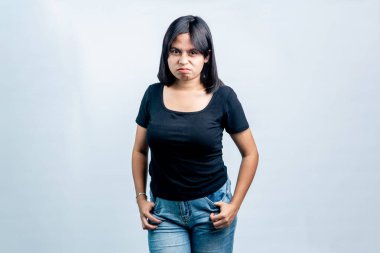 Kızgın ve huysuz bir ifadeyle genç bir Güneydoğu Asyalı kadının portresi, elleri ceplerinde, temiz beyaz bir stüdyo geçmişine karşı poz veriyor..