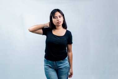 Siyah tişörtlü ve kot pantolonlu genç bir kadın, bir eli başının arkasında, temiz beyaz bir arkaplanda güven içinde poz veriyor..