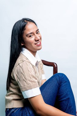 Uzun siyah saçlı mutlu bir Asyalı kadın, beyaz bir stüdyo arka planında parlak bir gülümseme ile omzunun üzerinden bakıyor..