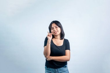 Siyah tişörtlü, kameraya gülümseyen ve bir parmağını yukarı kaldırıp beyaz bir arka planda izole edilmiş, dost canlısı bir Asyalı genç kadın..