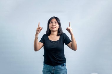 Siyah tişörtlü gülümseyen bir Asyalı kadın işaret parmaklarıyla yukarı bakıyor, beyaz bir arka planda izole edilmiş..
