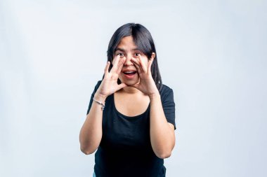 Siyah tişörtlü mutlu bir Asyalı kadın, elleri ağzının etrafında sanki beyaz bir arka planda bağırıyor ya da haber veriyor gibi poz veriyor..