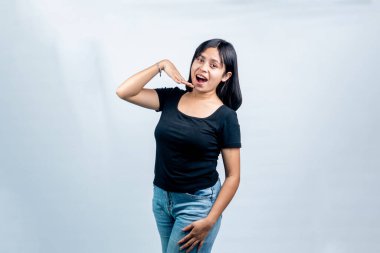 Siyah tişörtlü mutlu bir Asyalı kadın neşeli bir ifade takınıyor ve beyaz stüdyo geçmişine karşı coşkulu bir el hareketi yapıyor..