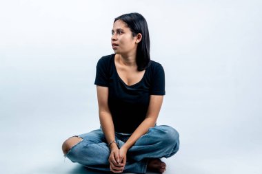 Beyaz arka planda oturan Güneydoğu Asyalı genç kadın başka tarafa bakıyor. Profesyonel stüdyoda siyah gömlekli ve kot pantolonlu sıradan bir Endonezyalı kız..