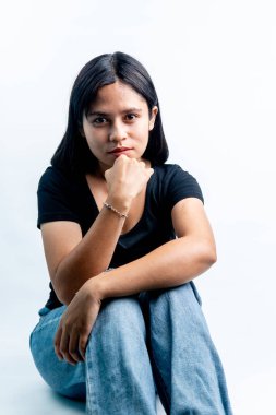 Güneydoğu Asyalı düşünceli kadın kameraya bakıyor. Beyaz arka planda siyah gömlek ve kot pantolon giyen Endonezyalı genç bir kadının portresi.