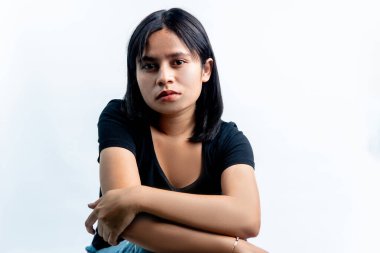 Siyah tişörtlü genç bir Güneydoğu Asyalı kadın portresi kollarını kavuşturmuş, beyaz arka planda sakin ve ciddi bir ifade sergiliyor..