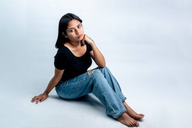 Siyah tişörtlü ve yerde oturan kendinden emin Güneydoğu Asyalı kadın. İzole edilmiş stüdyo görüntüleri beyaz, yansıma konsepti veya gençlik yaşam tarzı üzerine.