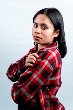 Ciddi bir Güneydoğu Asyalı kız öğrenci omzunun üzerinden kameraya bakıyor. Beyaz arka plan, gençlik konsepti ve kimlik üzerine izole edilmiş stüdyo görüntüleri..