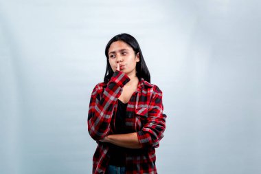 Kırmızı flanel gömlekli, ağzı parmaklarıyla sessizlik isteyen odaklanmış genç bir kadın. Beyaz arkaplan üzerine stüdyo çekimi, sessizlik ve odaklanma kavramı.