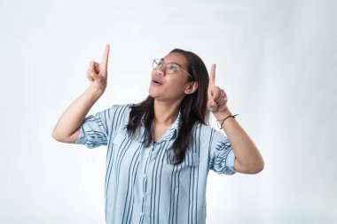 Endonezyalı gözlüklü ve çizgili tişörtlü heyecanlı genç bir kadın, şaşırmış bir ifadeyle işaret ediyor. Büyük haberler ve indirimler için ideal..