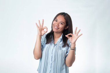 Çizgili tişörtlü mutlu bir Endonezyalı kadın gülümsüyor ve el işareti yapıyor. Anlaşma, kalite ve memnuniyet kavramı.