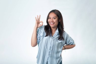 Çizgili tişörtlü mutlu bir Endonezyalı kadın gülümsüyor ve el işareti yapıyor. Anlaşma, kalite ve memnuniyet kavramı.