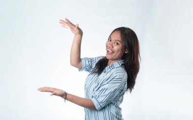 Çizgili tişörtlü neşeli genç Endonezyalı bir kadın bir ürün ya da metin sunmak için avuç içi açık el kol hareketi yapıyor. Reklam ve kopyalama alanı kavramı.