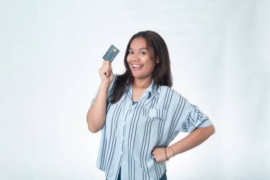 Mutlu bir Endonezyalı kadın kredi kartını kendine güvenen bir pozla gösteriyor. Kişisel finans, bankacılık başarısı ve bağımsız yaşam tarzı reklamları için harika..