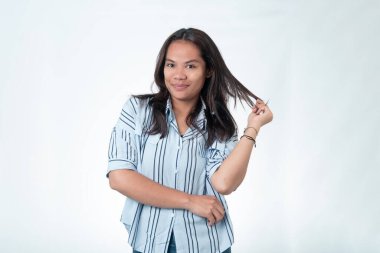 Çekici Endonezyalı mavi çizgili tişörtlü bir kadının portresi. Bir tutam saçını çevirirken kameraya gülümsüyor. Kendine güvenen ve flört eden ifade, beyazda soyutlanmış..