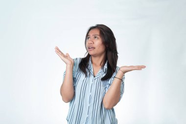 Endonezyalı mavi çizgili gömlekli bir kadının portresi omuzlarını silkiyor ve kafası karışmış bir ifadeyle yukarı bakıyor. Beyazda izole edilmiş.