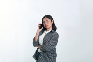 Kulağına telefon tutan ekose gömlekli Endonezyalı bir kadının portresi. Düşünceli bir ifadeyle yukarıya bakıyor. Beyazda izole edilmiş.