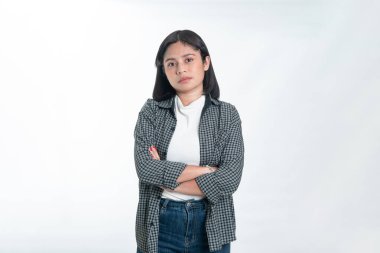 Ekose gömlek ve kot pantolon giymiş Endonezyalı bir kadının portresi. Kollarını kavuşturmuş ve tarafsız, kendinden emin bir ifadeyle duruyorsun. Beyazda izole edilmiş.