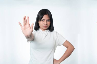 Beyaz tişörtlü Endonezyalı genç bir kadının portresi avucunu ileri doğru uzatarak dur işareti yapıyor. Seçici odaklanma, odaklanma ve biraz bulanıklaşma. Beyaz arkaplanda izole.