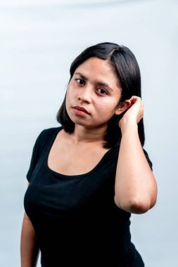 Siyah tişörtlü sakin bir Endonezyalı kadının, objektif ve düşünceli bir ifadeyle kameraya bakışının portresi. Beyaz stüdyo arka planında izole edilmiş..