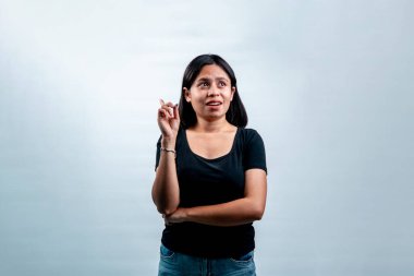 Endonezyalı genç bir kadın farkında olmadan başka tarafa bakıyor ve bir parmağını havaya kaldırıyor. Cömert kopya alanı olan beyaz arkaplanda izole edilmiş.