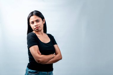 Sıradan siyah tişörtlü genç bir Endonezyalı kadın kollarını kavuşturmuş ve kendinden emin bir ifadeyle ayakta duruyor. İş ve yaşam tarzı temaları için ideal.