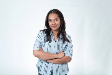 Kollarını kavuşturmuş mavi çizgili tişörtlü Endonezyalı genç bir kadının portresi. İnce, kendinden emin bir gülüşü var ve beyaz bir arka planda izole edilmiş..